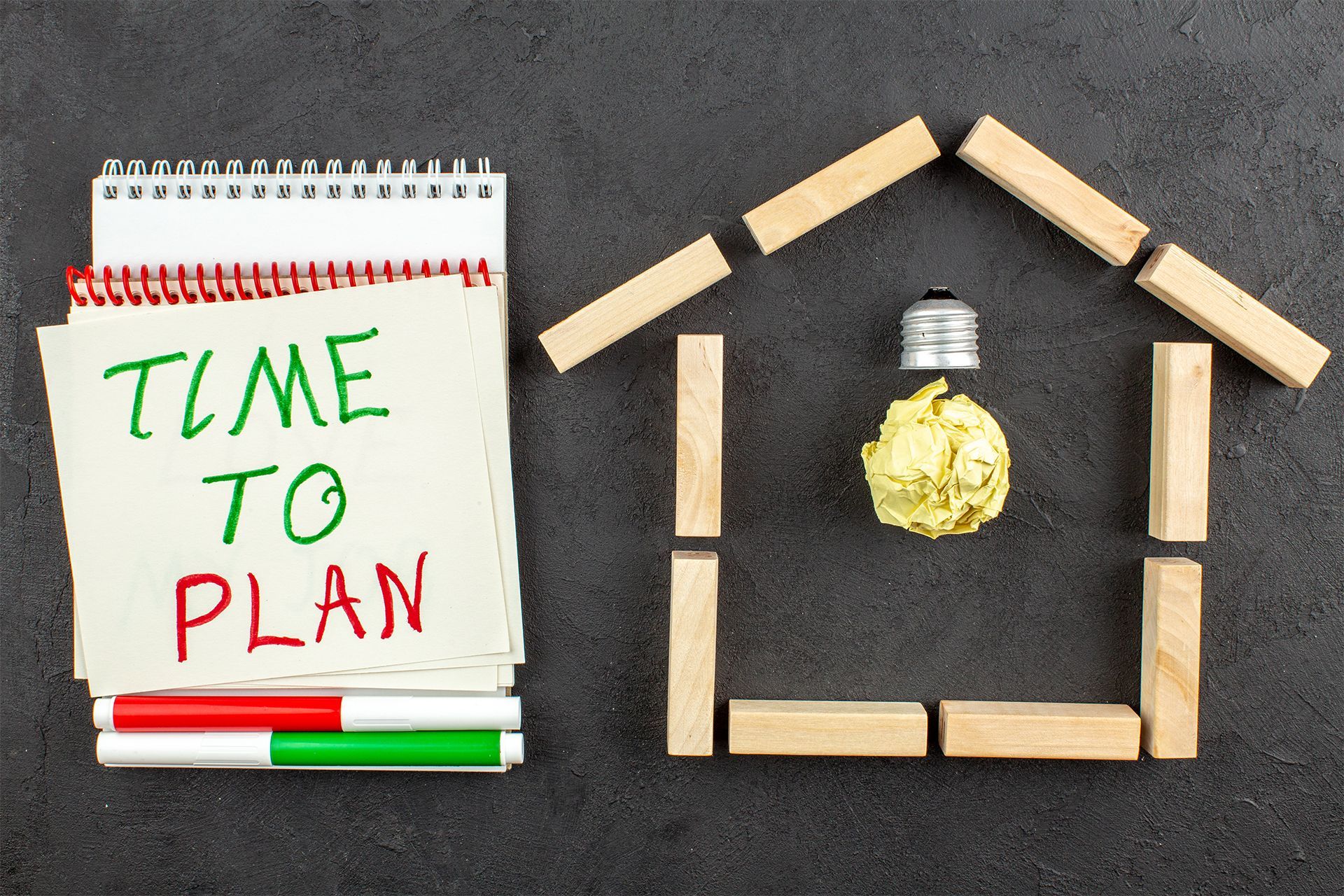 A notepad and a house shape made of wooden blocks with a lightbulb inside.