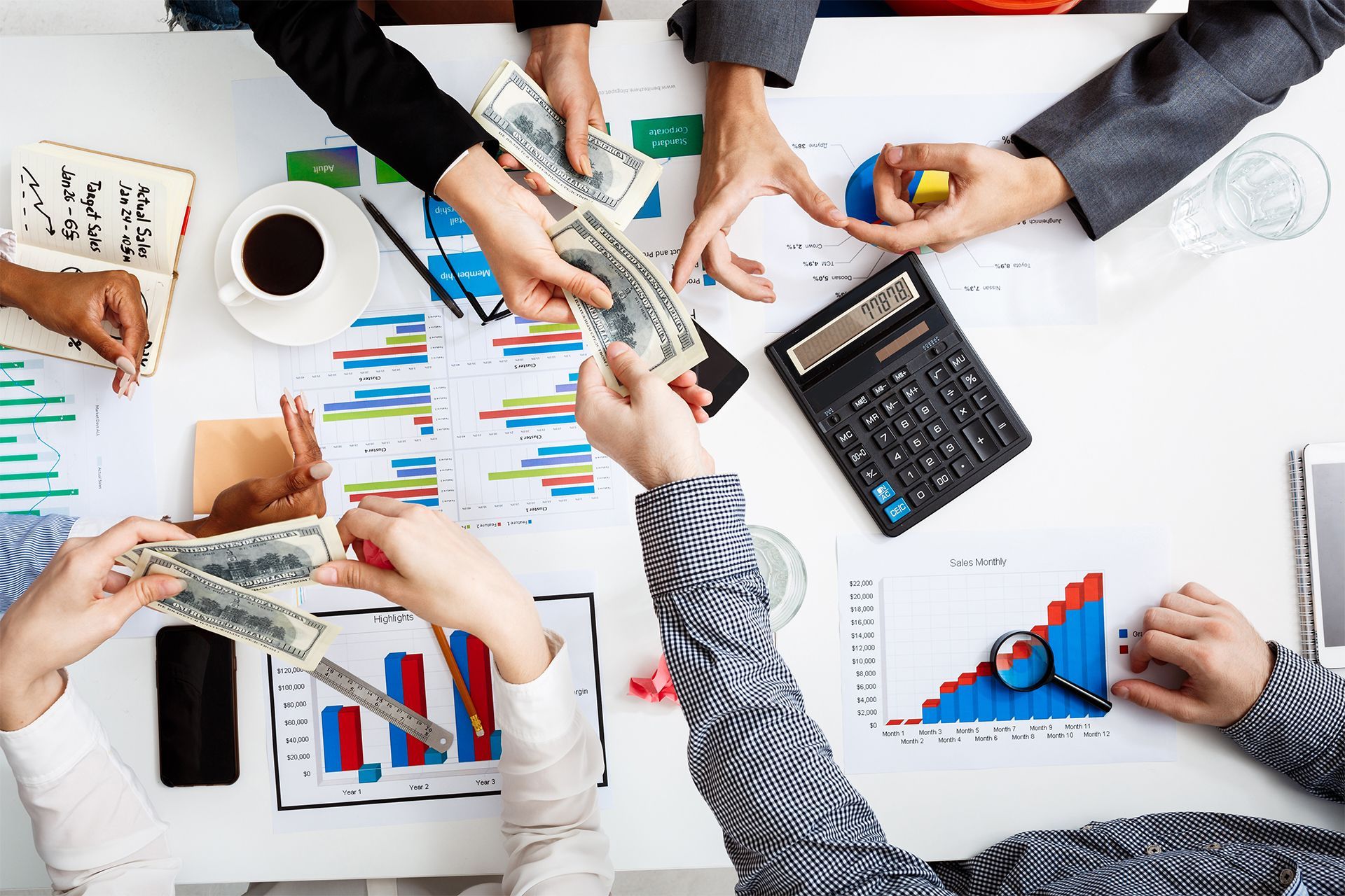 Hands Sharing Money Over a Table With Charts Representing Financial Collaboration