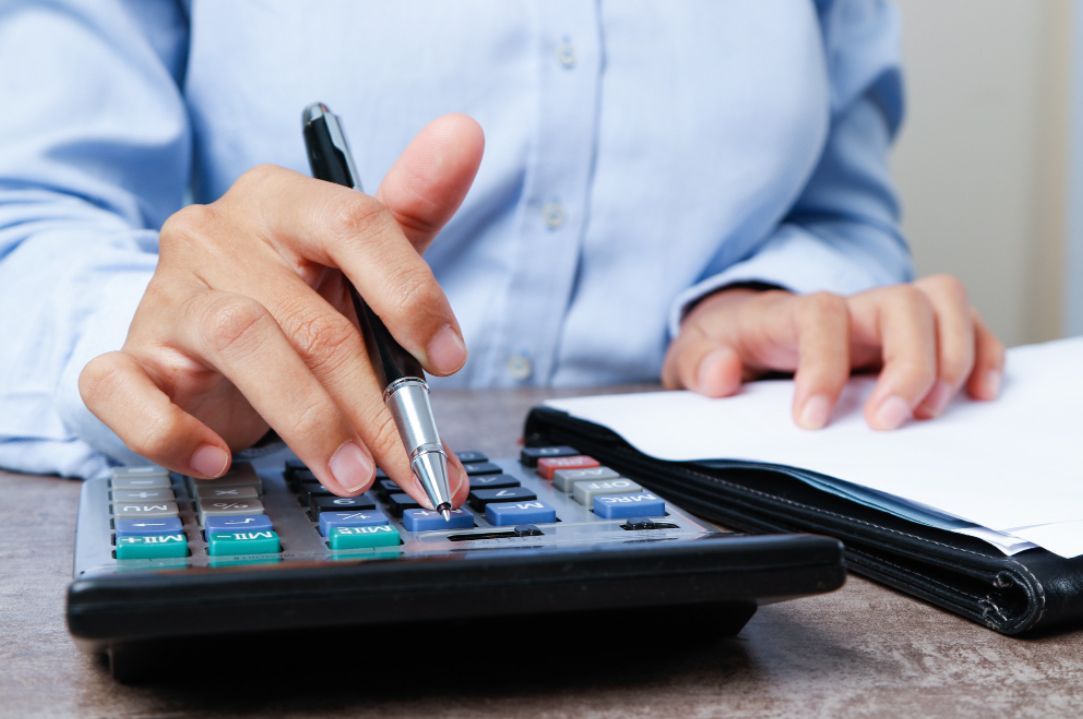 Person's hands using a calculator, with pen on a desk near paperwork, in a close up shot.