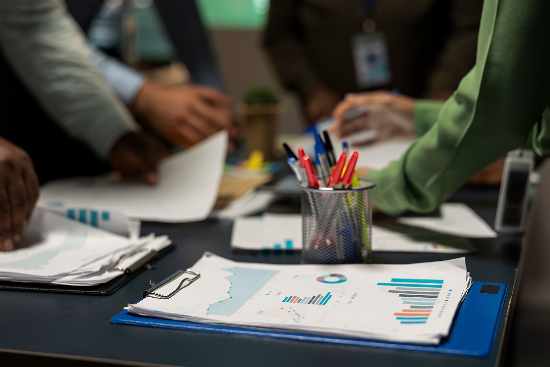 Team members reviewing charts and papers around a table. Team members reviewing charts and papers around a table.