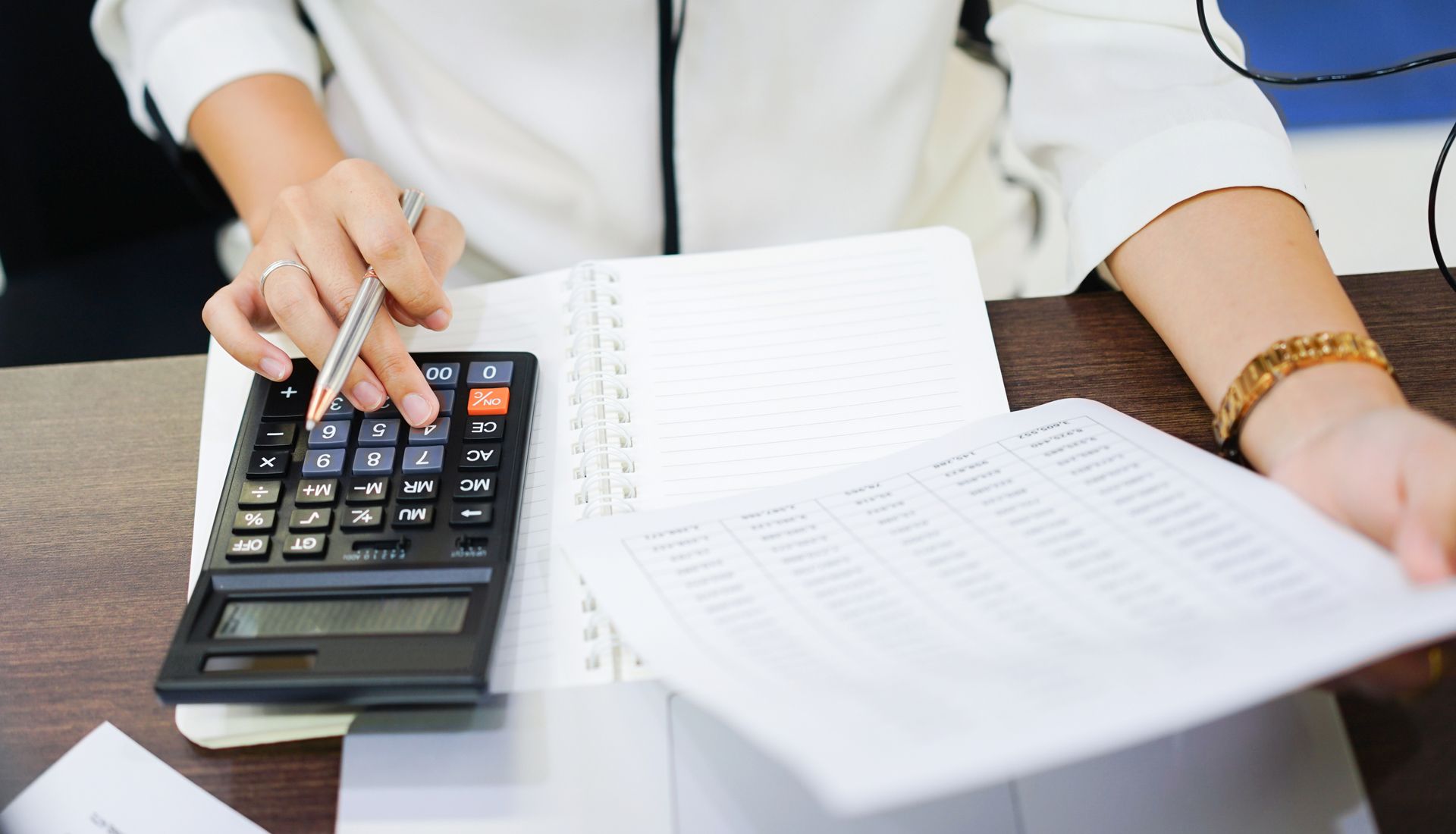 A woman is sitting at a desk using a calculator and a pen.