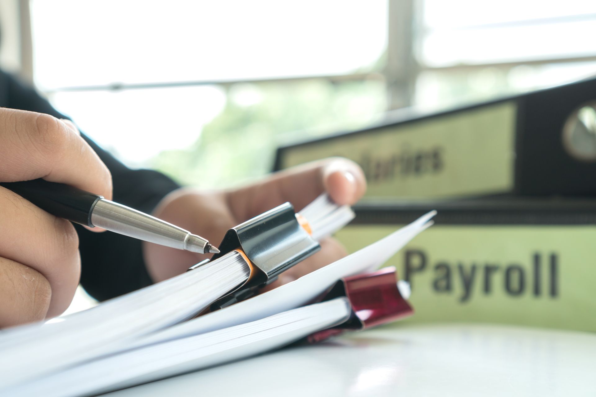 A Person is Holding a Pen Over a Stack of Papers