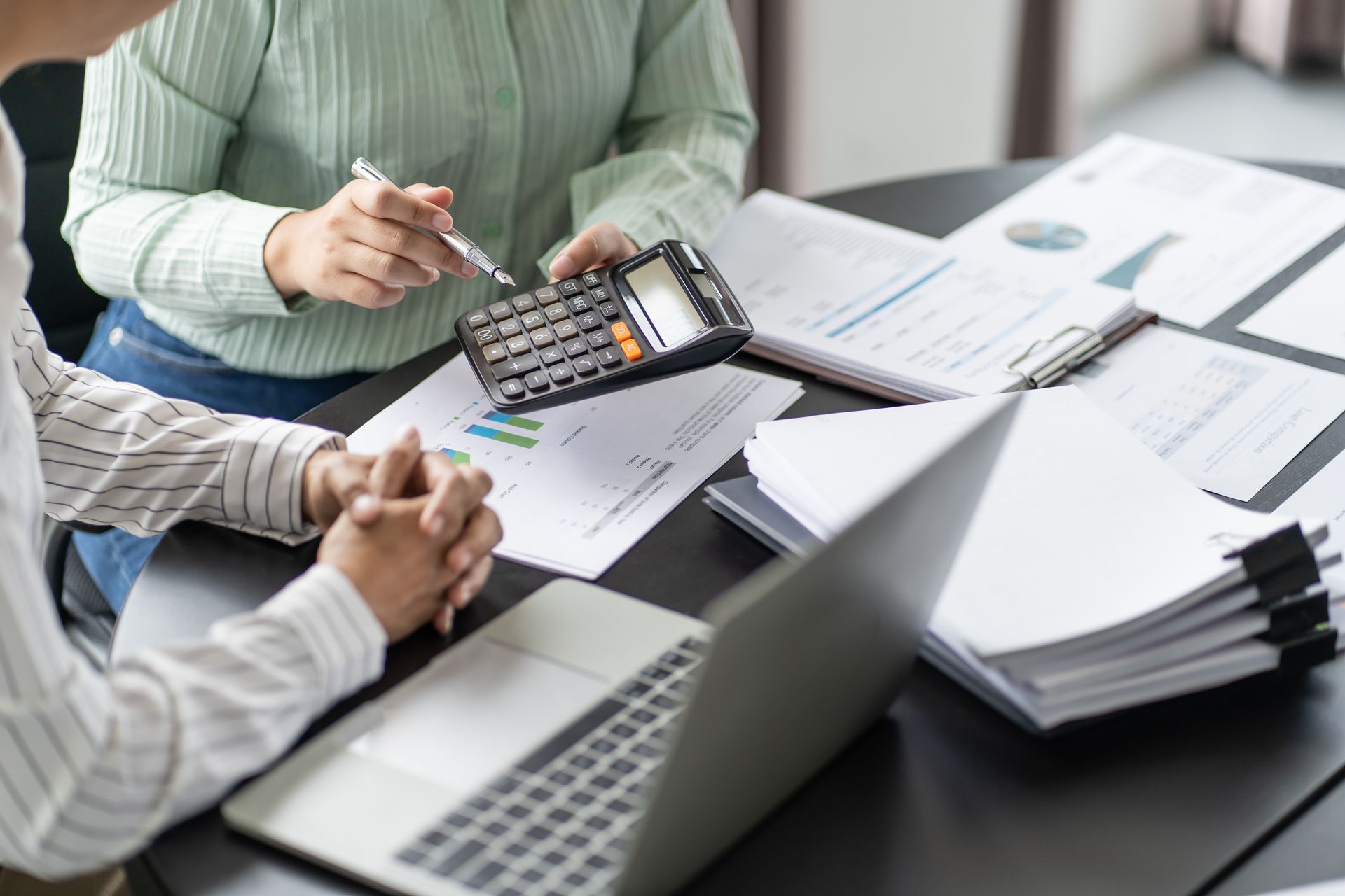 Two people reviewing financial documents at a desk with a calculator and laptop.