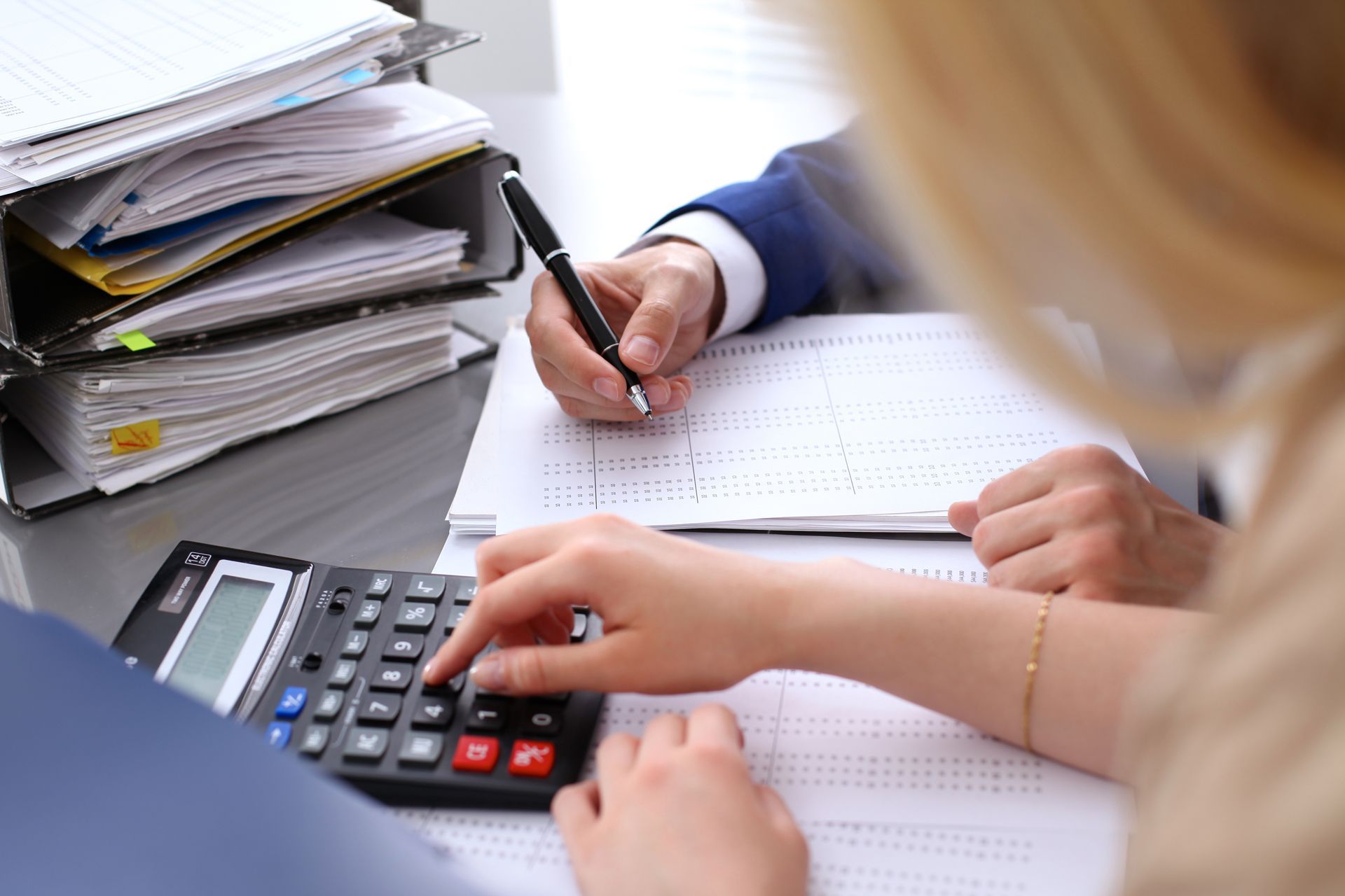 A Woman is Using a Calculator While a Man is Writing on a Piece of Paper.