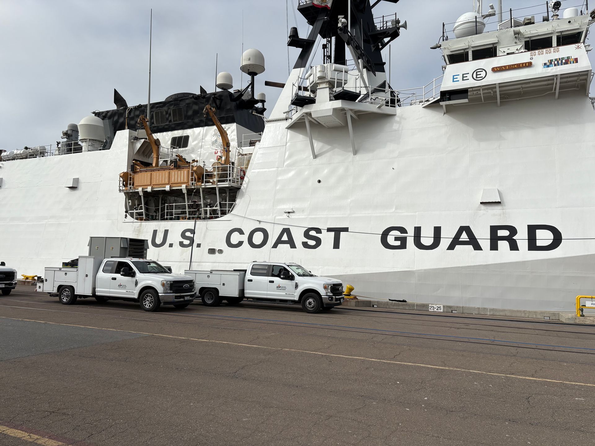 Two white Coast Guard trucks parked next to a large white Coast Guard ship.