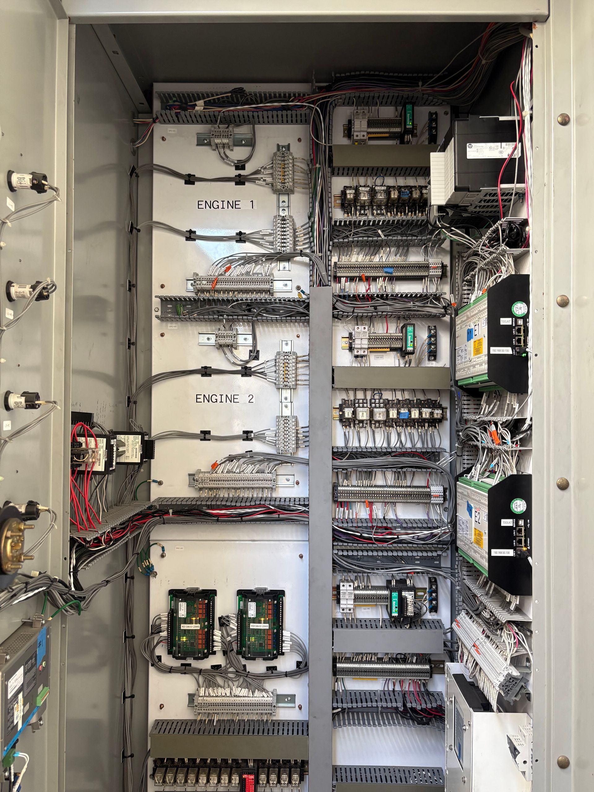 Electrical control panel with numerous wires, relays, and circuit breakers inside a gray cabinet.