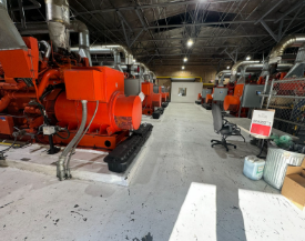 Row of large orange industrial generators in a brightly lit warehouse.