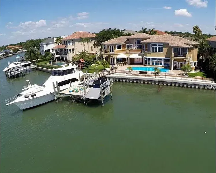 An aerial view of a large house next to a body of water with boats docked.