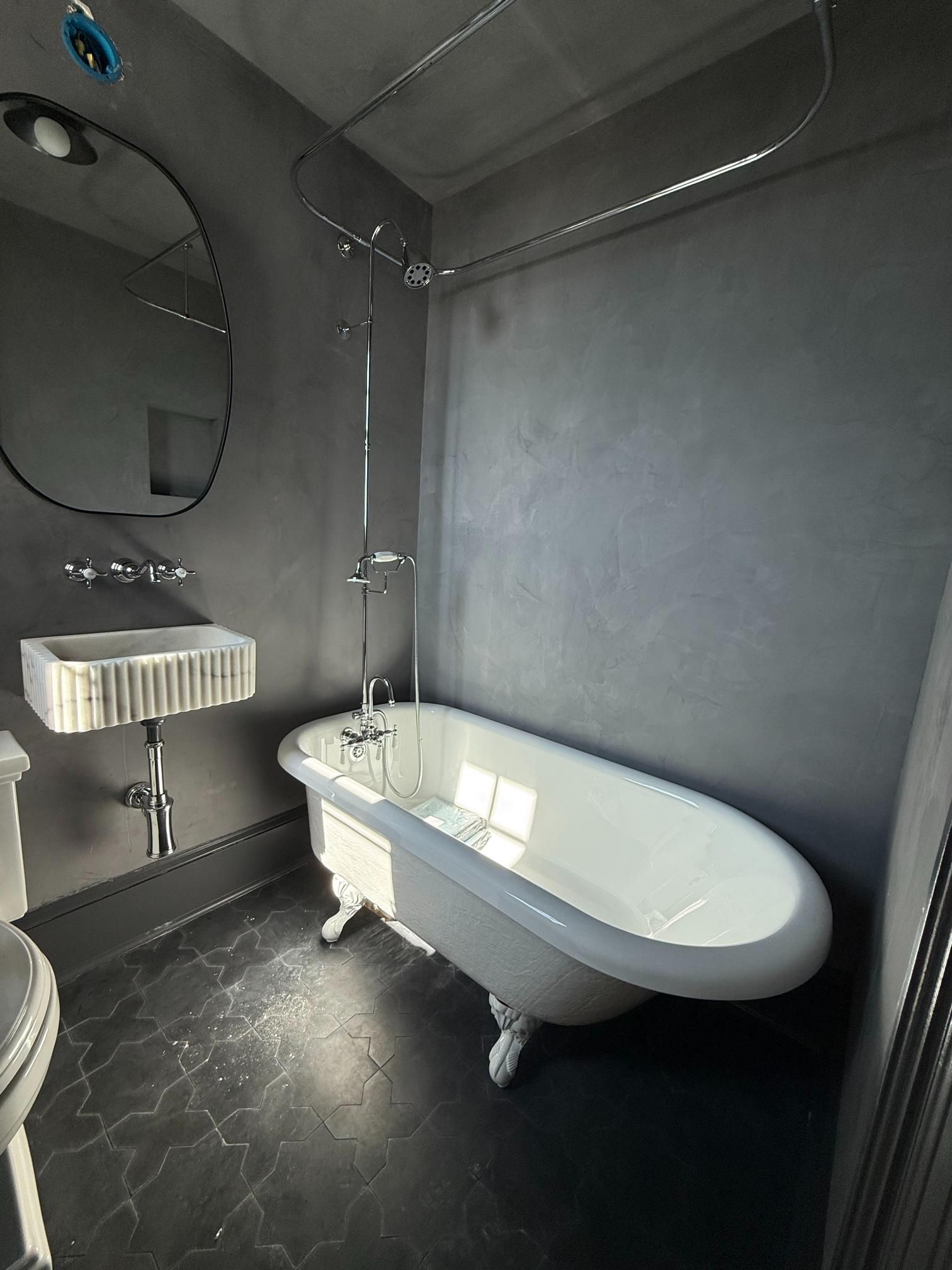 Gray bathroom with a white clawfoot tub, sink, and mirror; dark floor.
