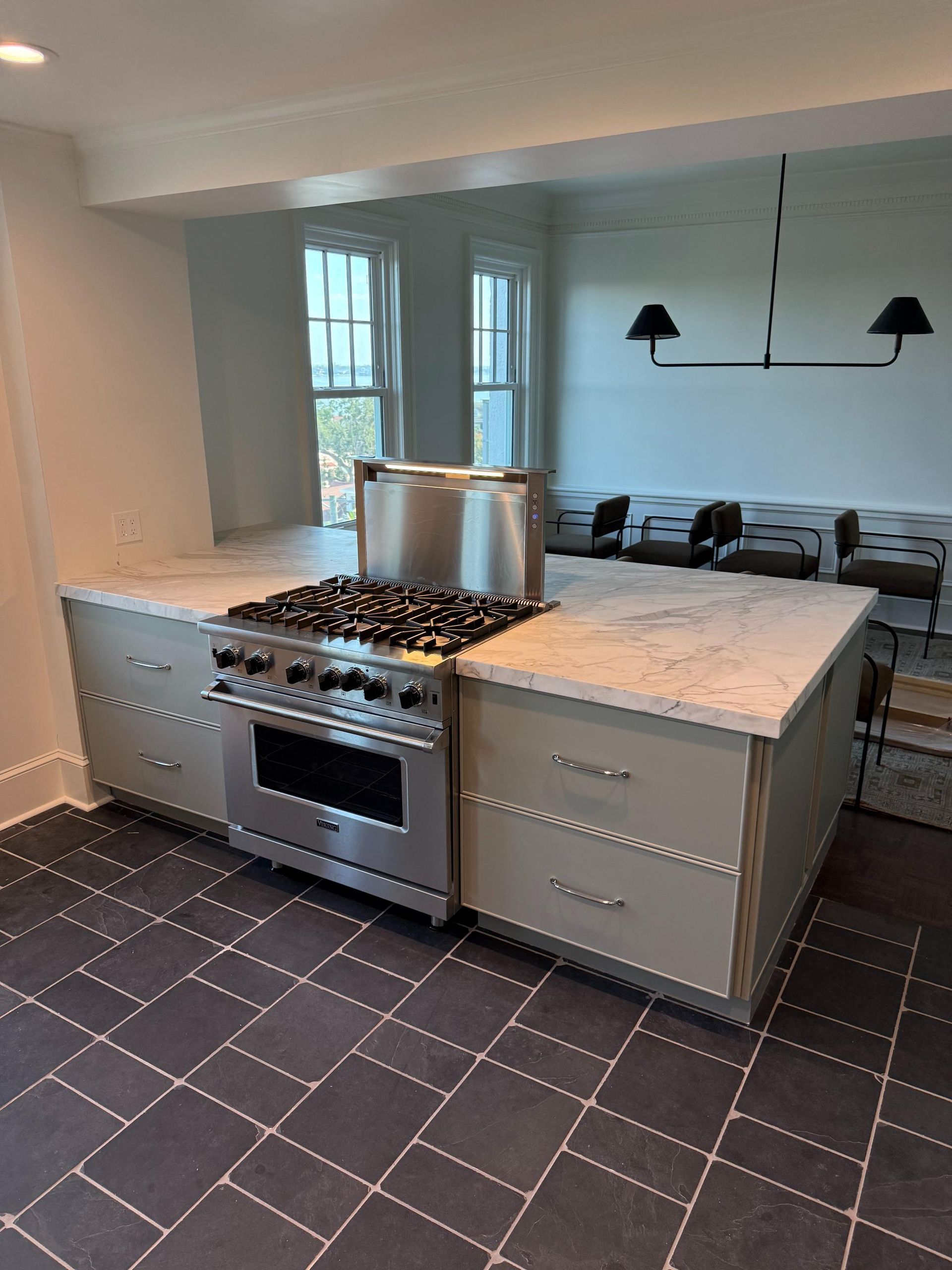Kitchen island with stainless steel stove and range hood, beige cabinets, and light countertop.