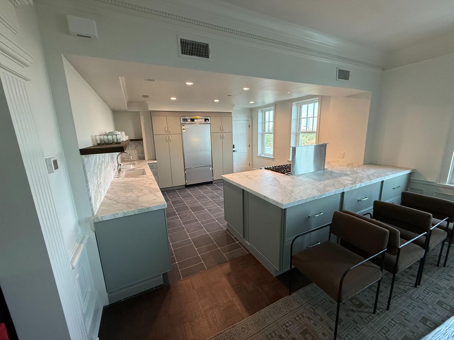 Spacious modern kitchen with island and light grey cabinetry, stainless steel appliances, and dark floor tiles.