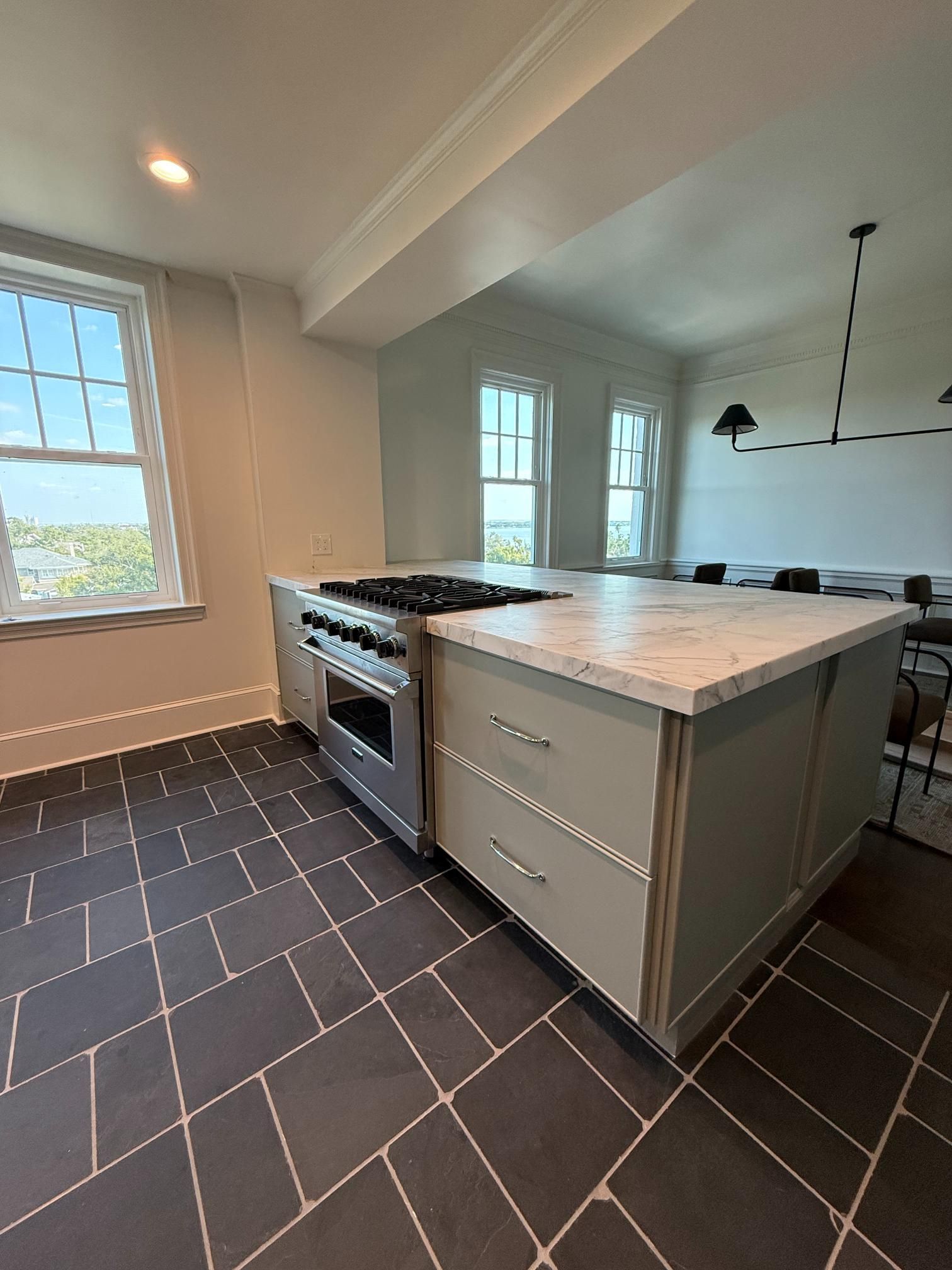Kitchen with a stove/oven island, marble countertop, dark tiled floor, and windows.