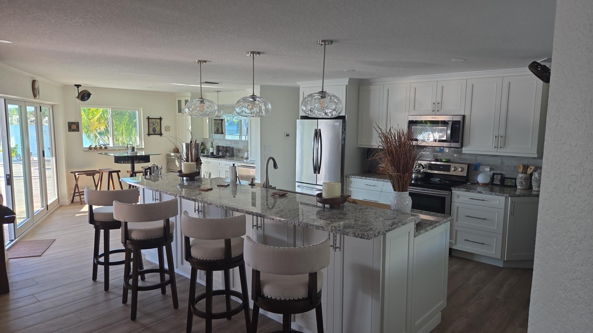Bright, open kitchen with white cabinets, island seating, pendant lights, and stainless steel appliances.