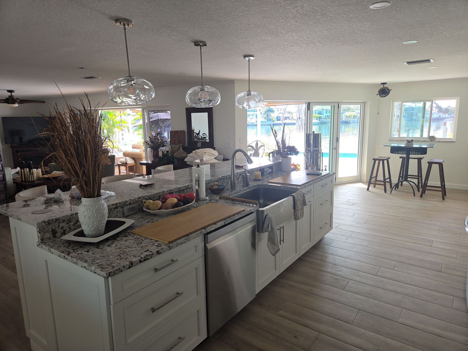 Kitchen with large island, pendant lights, and stainless steel sink, near sliding glass doors to pool.