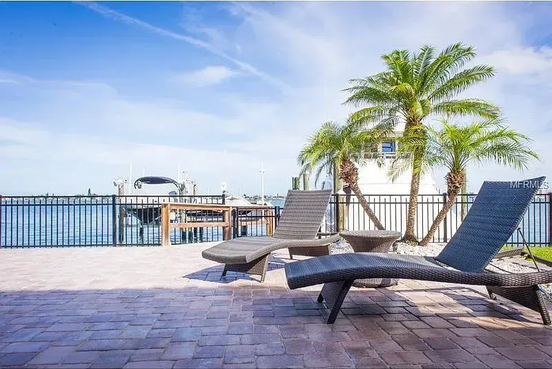 A patio with lounge chairs and palm trees overlooking the ocean.