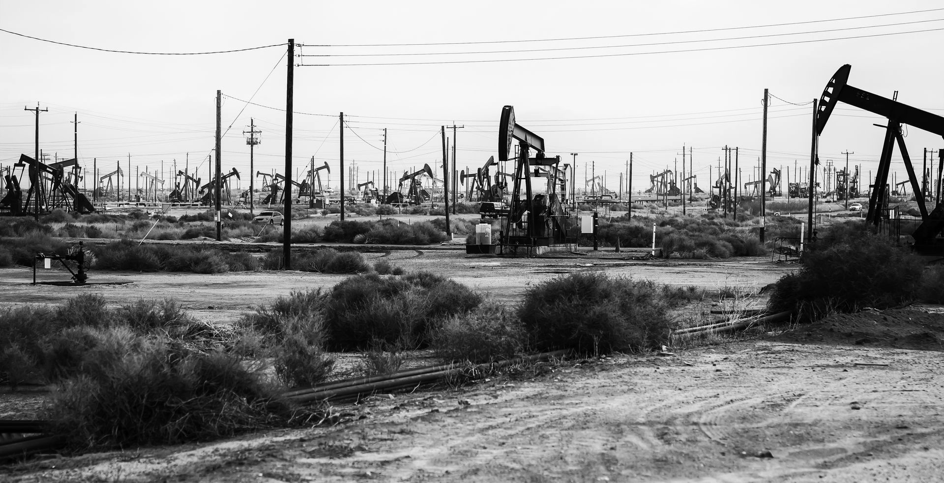 Oil pumps in a dry, open field under a cloudy sky.