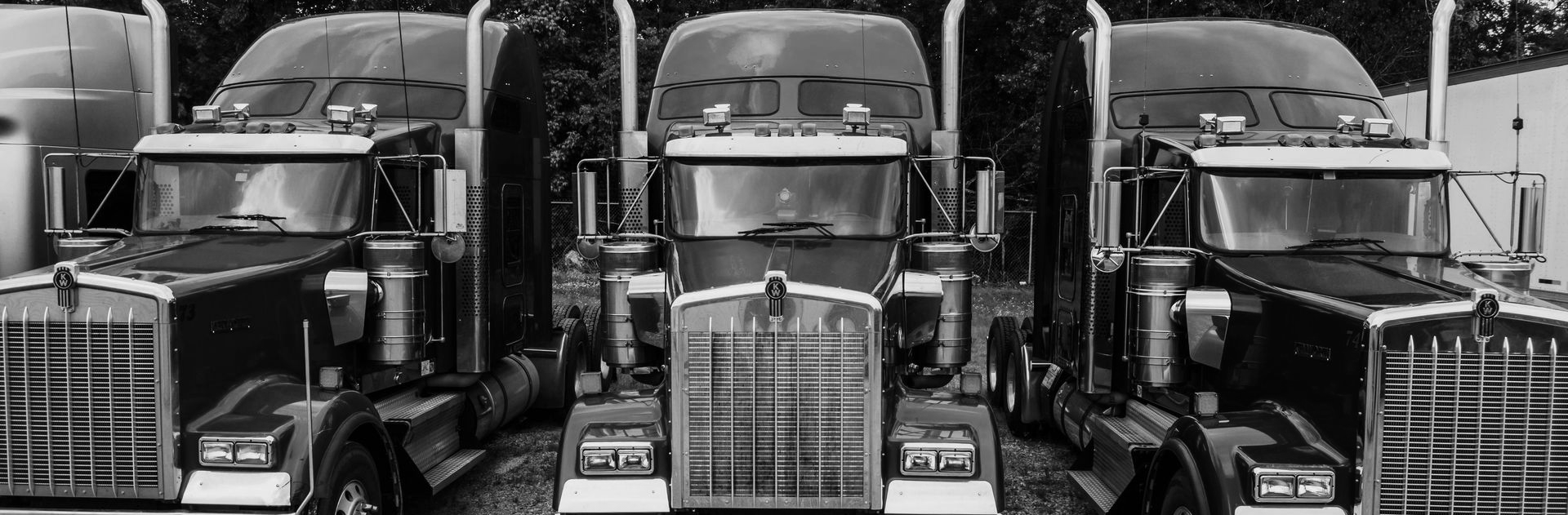 Three black and white semi-trucks parked side by side.