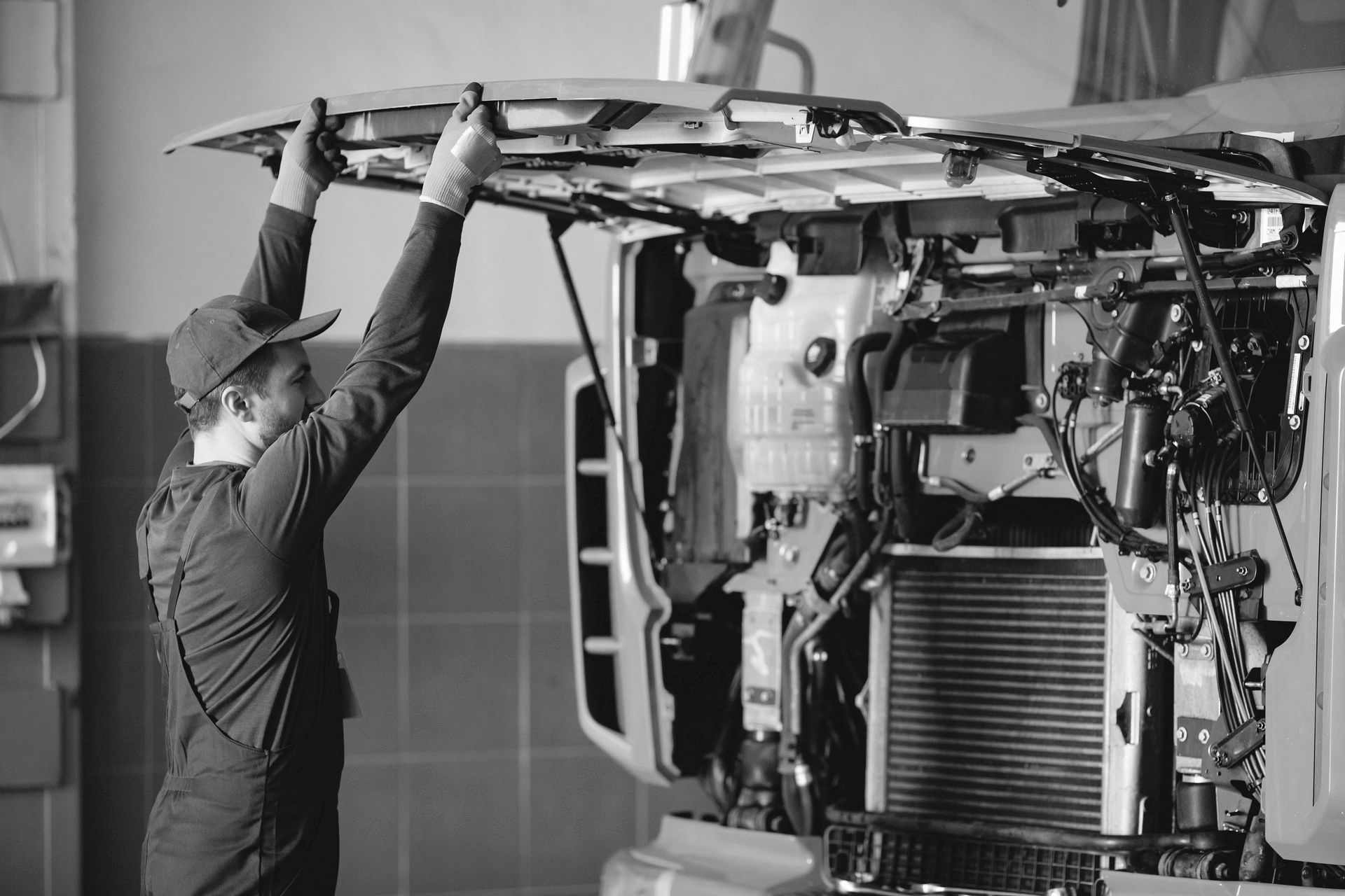 Mechanic holding a vehicle's front panel, revealing engine components in a repair shop.