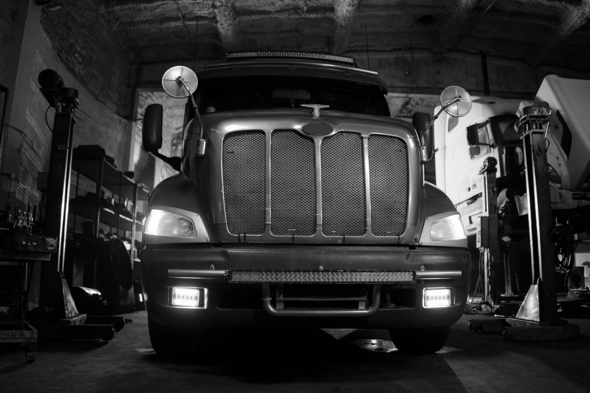 Black and white shot of a semi-truck in a garage, illuminated by its headlights and overhead lights.
