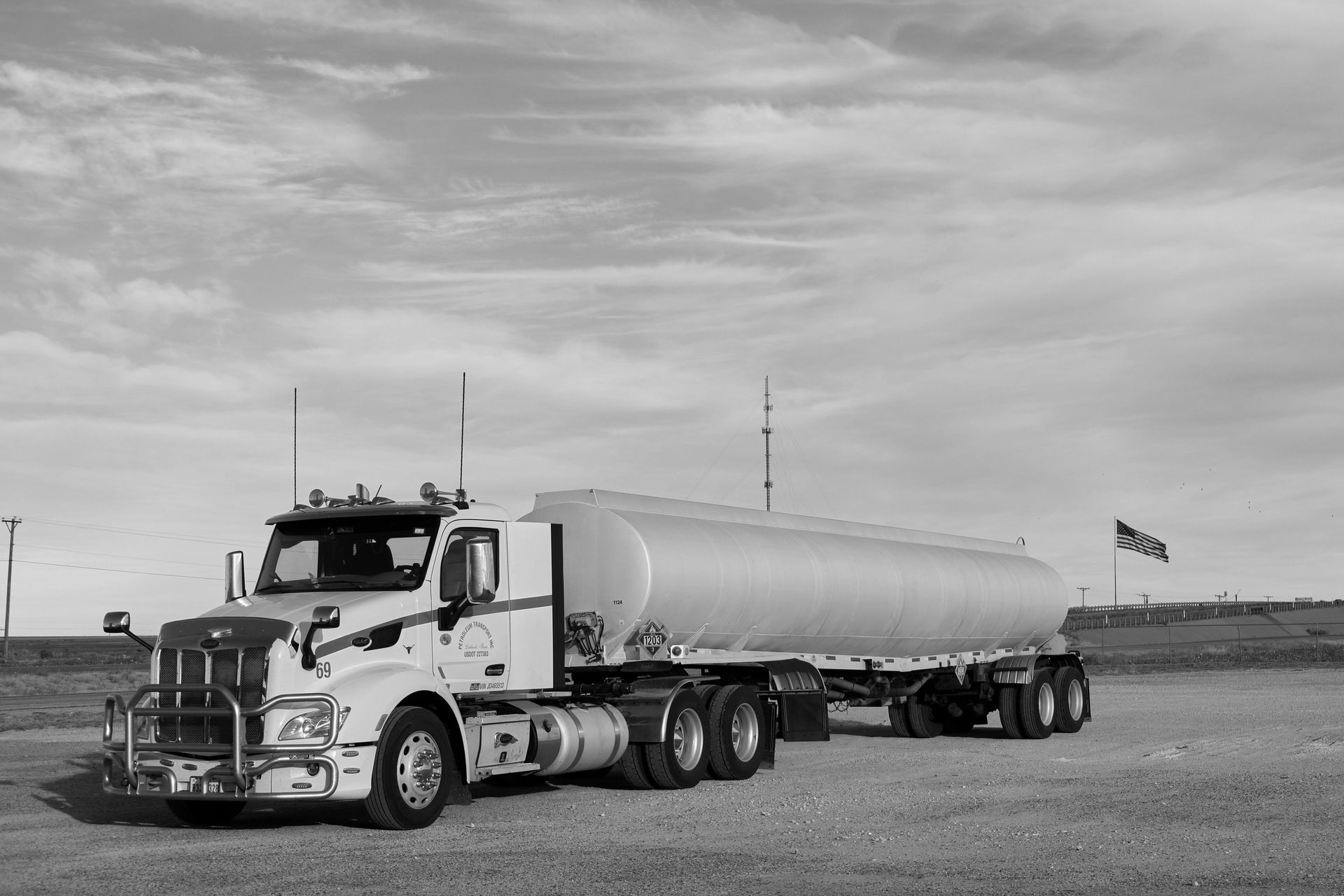 Semi-truck with tanker trailer parked on a gravel lot under a cloudy sky.