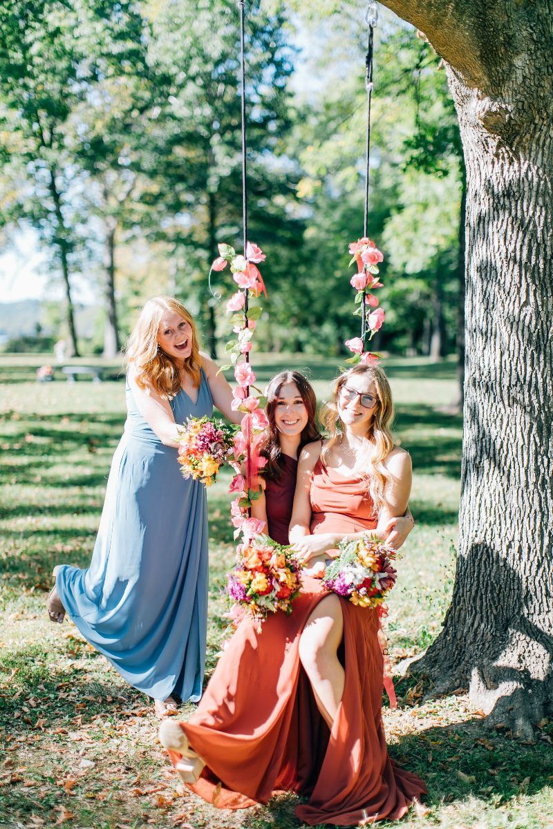 three women sitting on a swing with flowers hanging from it