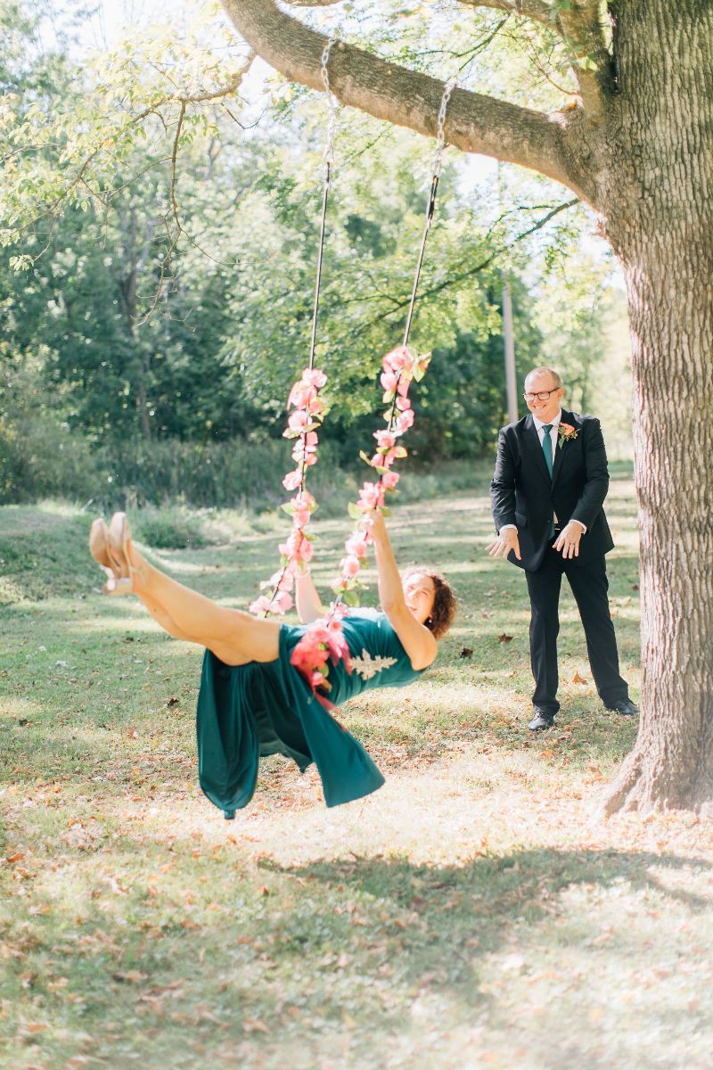 a bride in a green dress is swinging on a tree swing