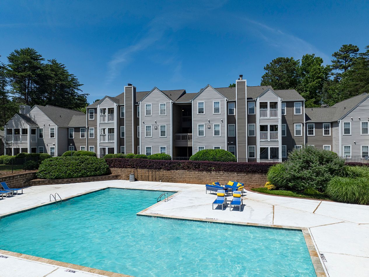 Apartment complex with a blue swimming pool and lounge chairs on a sunny day.