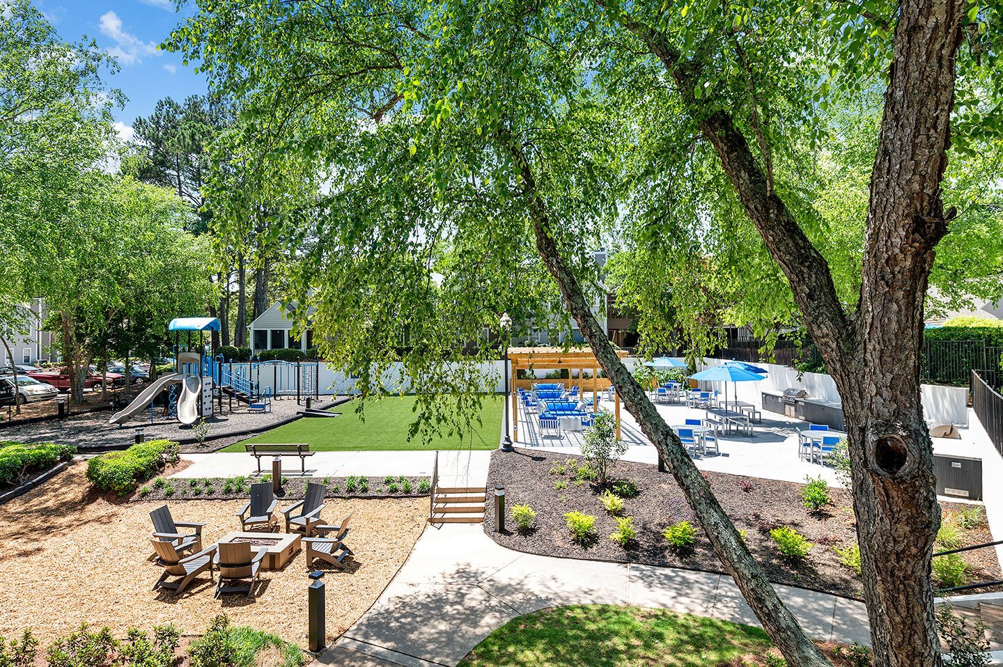 A landscaped outdoor area featuring a playground, pool with lounge chairs, and seating area with a fire pit at Station Heights in Alpharetta, GA.