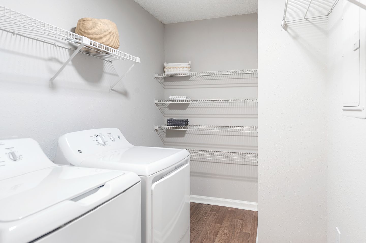 Laundry room with a white washer and dryer, shelving with items, and hardwood floors at Station Heights in Alpharetta, GA.