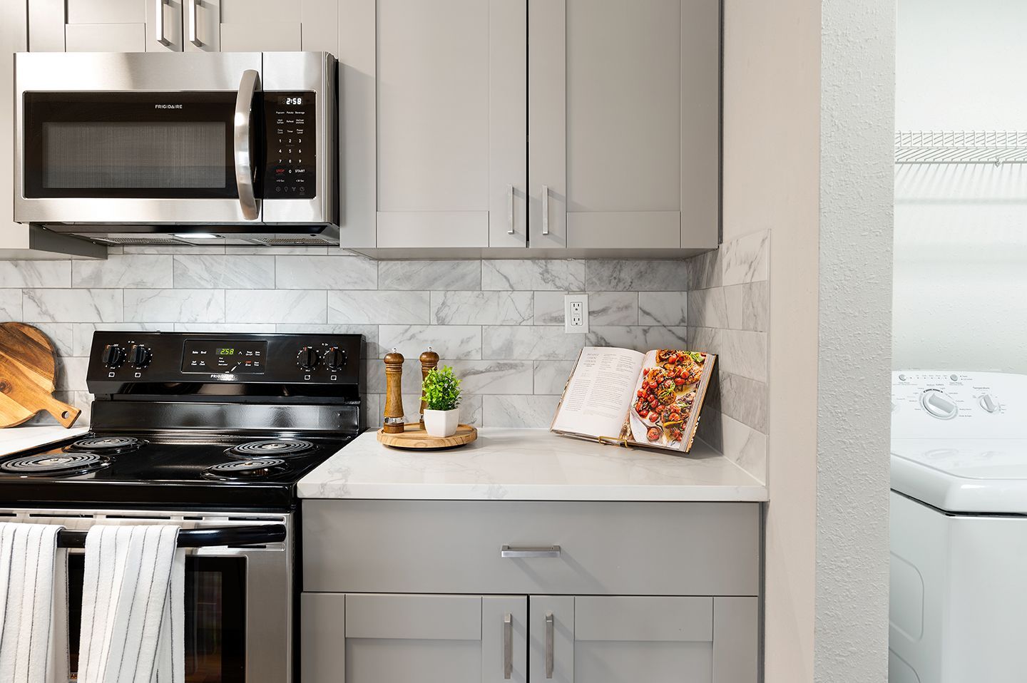 Gray kitchen with stainless steel appliances, marble backsplash, and open cookbook at Station Heights in Alpharetta, GA.