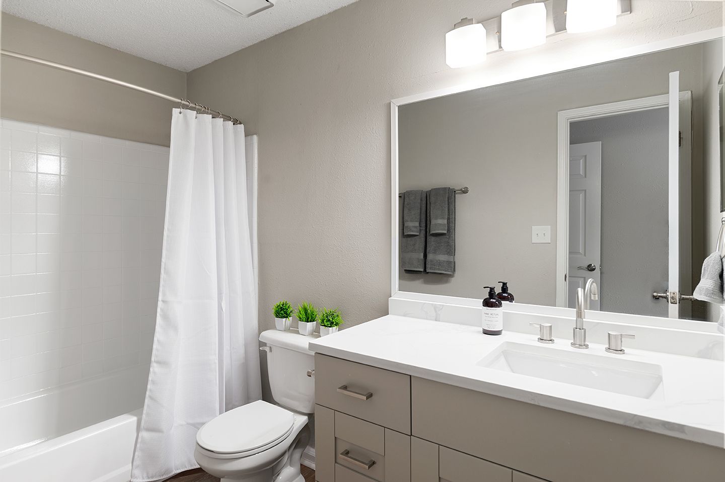 Bathroom with white vanity, tub, toilet, and gray walls; lit by overhead lights at Station Heights in Alpharetta, GA.