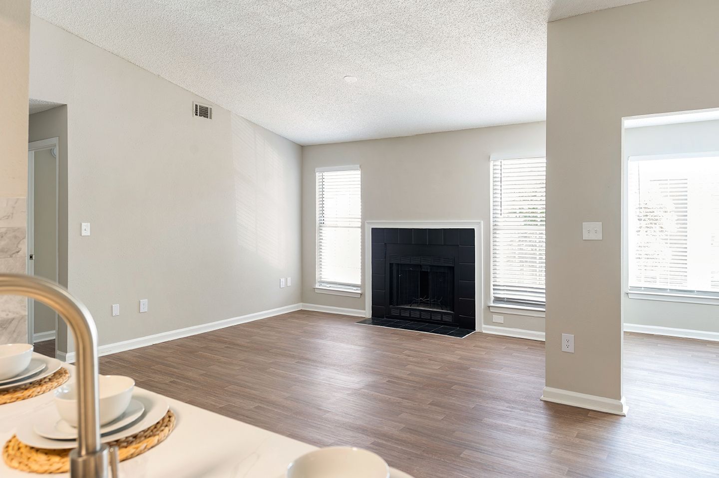 Empty living room with fireplace and two windows, light grey walls, and wood flooring at Station Heights in Alpharetta, GA.