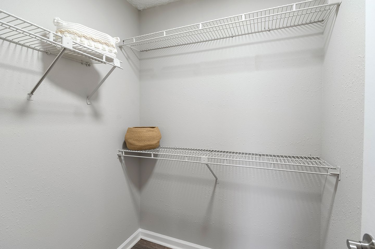 Empty wire shelving in a walk-in closet with a neutral-colored walls and a small bag at Station Heights in Alpharetta, GA.