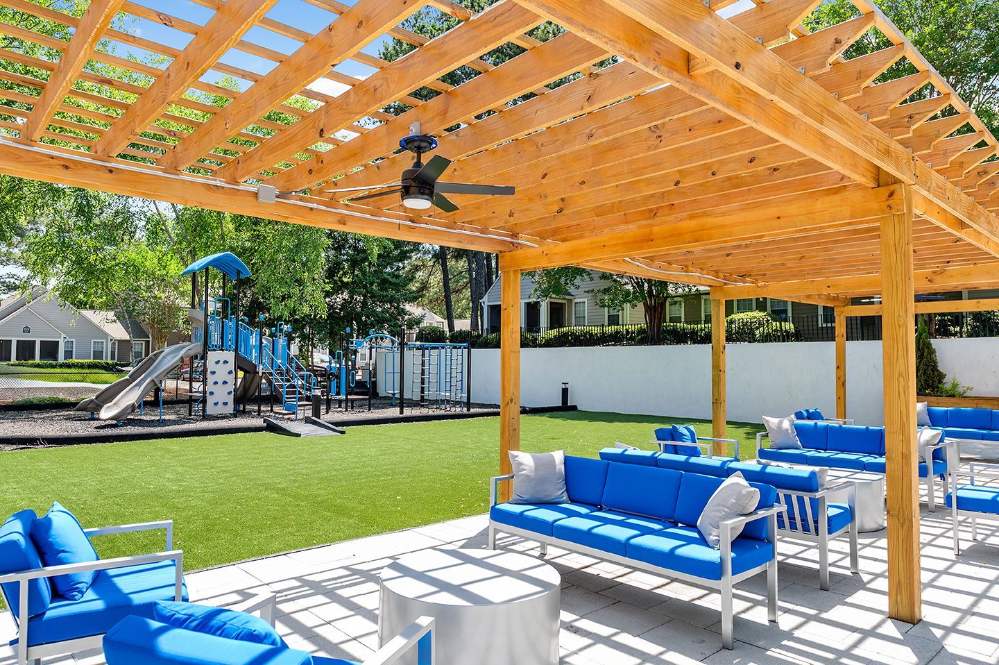 Outdoor seating area with blue couches under a wooden pergola, overlooking a playground.
