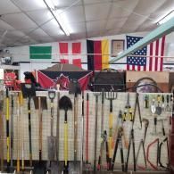 Wall of various yard and garden tools mounted on grid panels under a row of international flags.