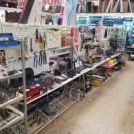 A cluttered aisle in a hardware store featuring shelves and pegboards packed with various tools, equipment, and supplies.