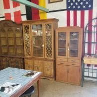 Three wooden cabinets stand in a room in front of flags, next to a table with a blue tiled surface.