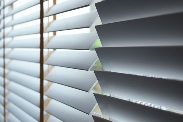 Close-up view of white, angled window blinds filtering sunlight.