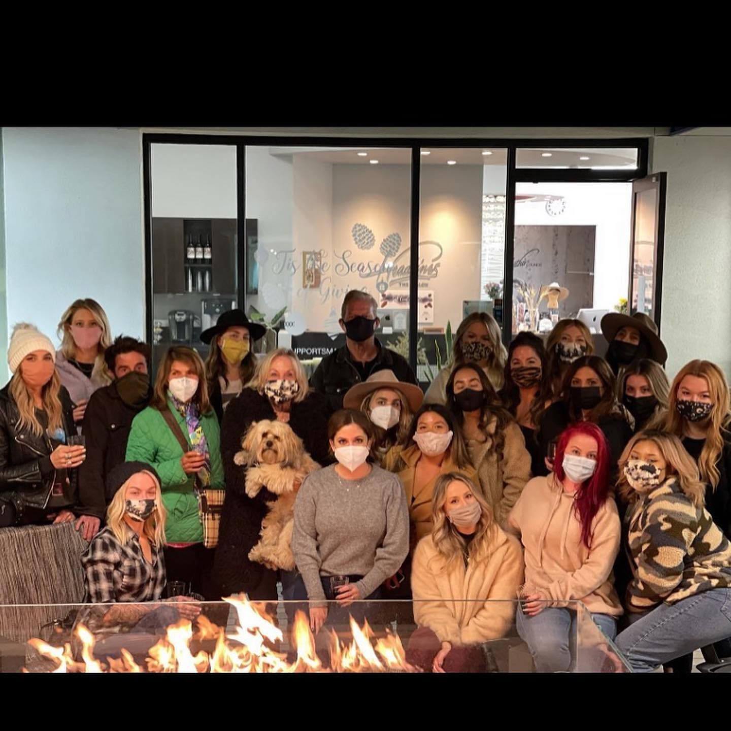 Group of people wearing masks, posing by an outdoor fire. Building with the words 