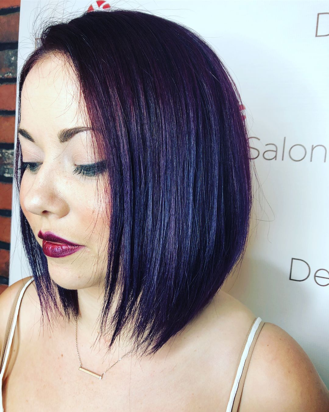 Woman with a purple bob hairstyle, dark lipstick, and a delicate necklace.