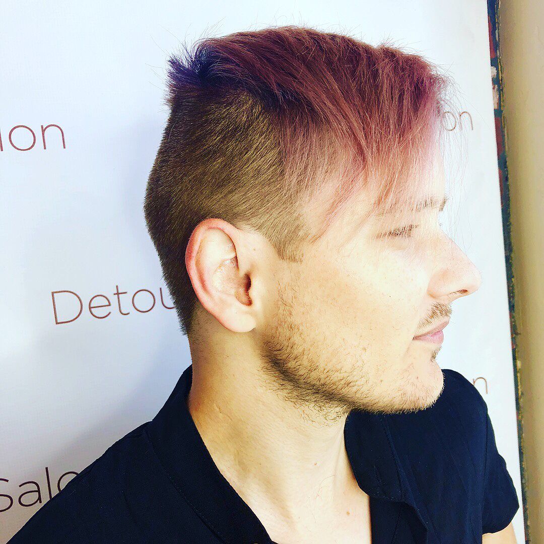 Man with burgundy hair and shaved sides, in front of a white salon wall.