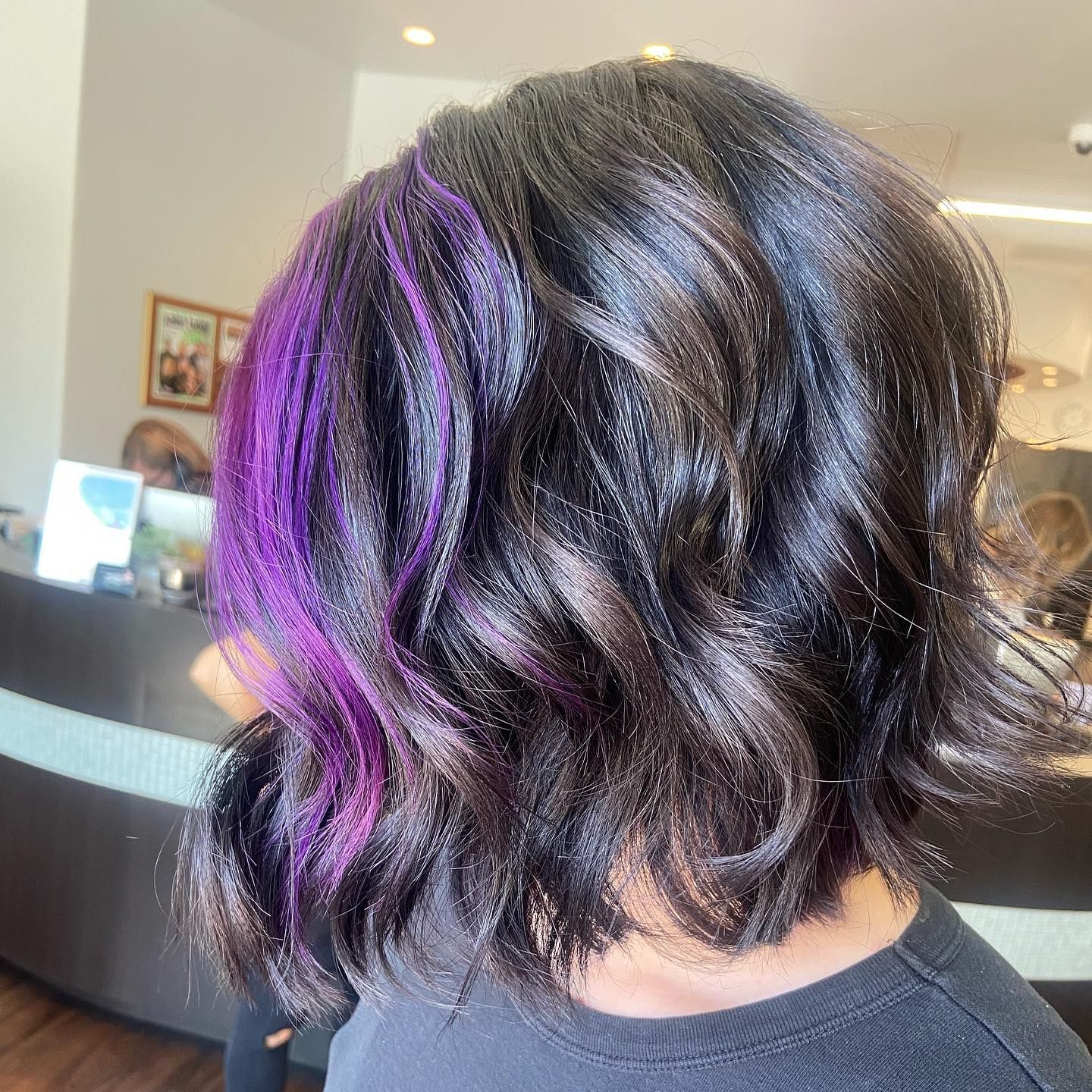 Woman with dark wavy hair, vibrant purple highlights on the side.