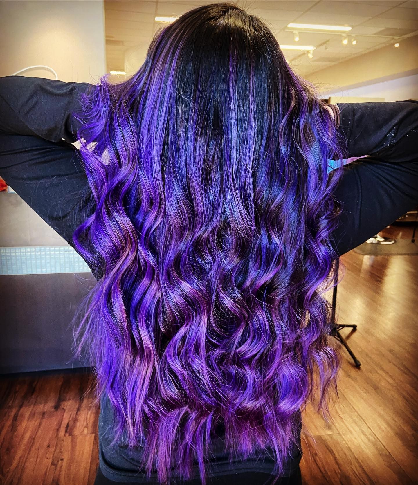 Long, wavy black hair with vibrant purple ombre, person with arms raised.