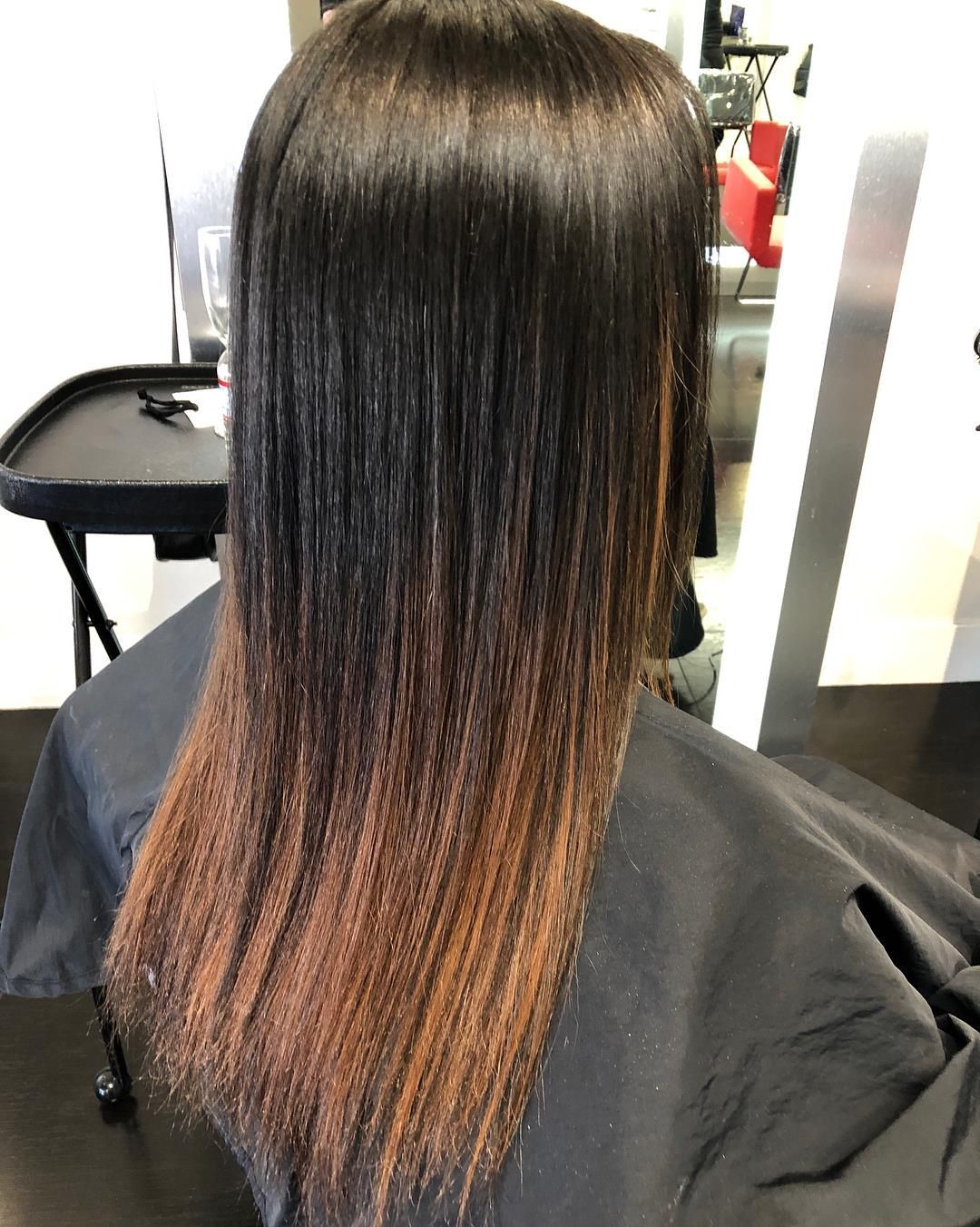 Black hair transitioning to brown, straightened. Salon setting, cape.