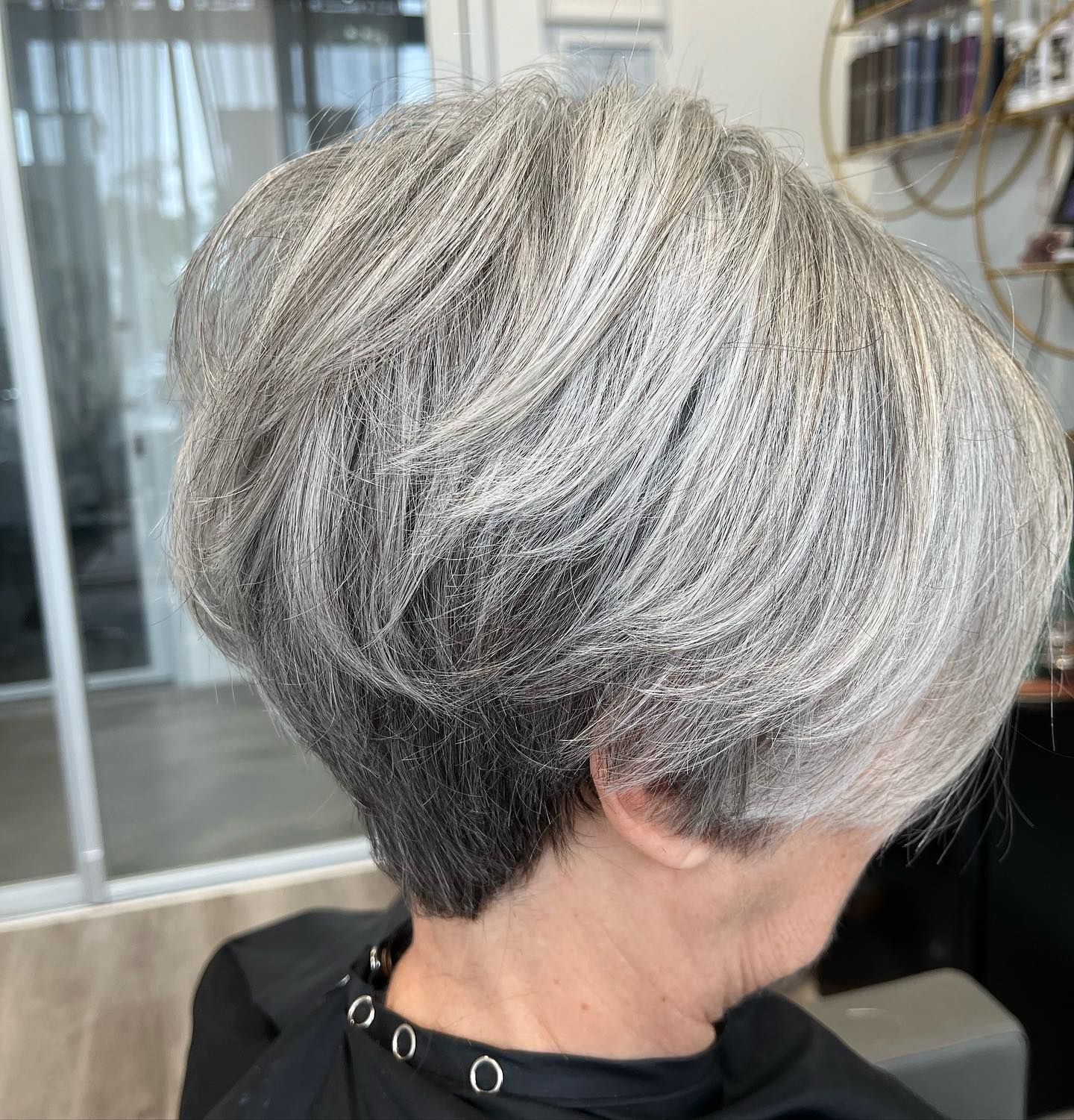 Close-up of a person's back, showcasing a layered, silver-gray pixie haircut with a dark nape.