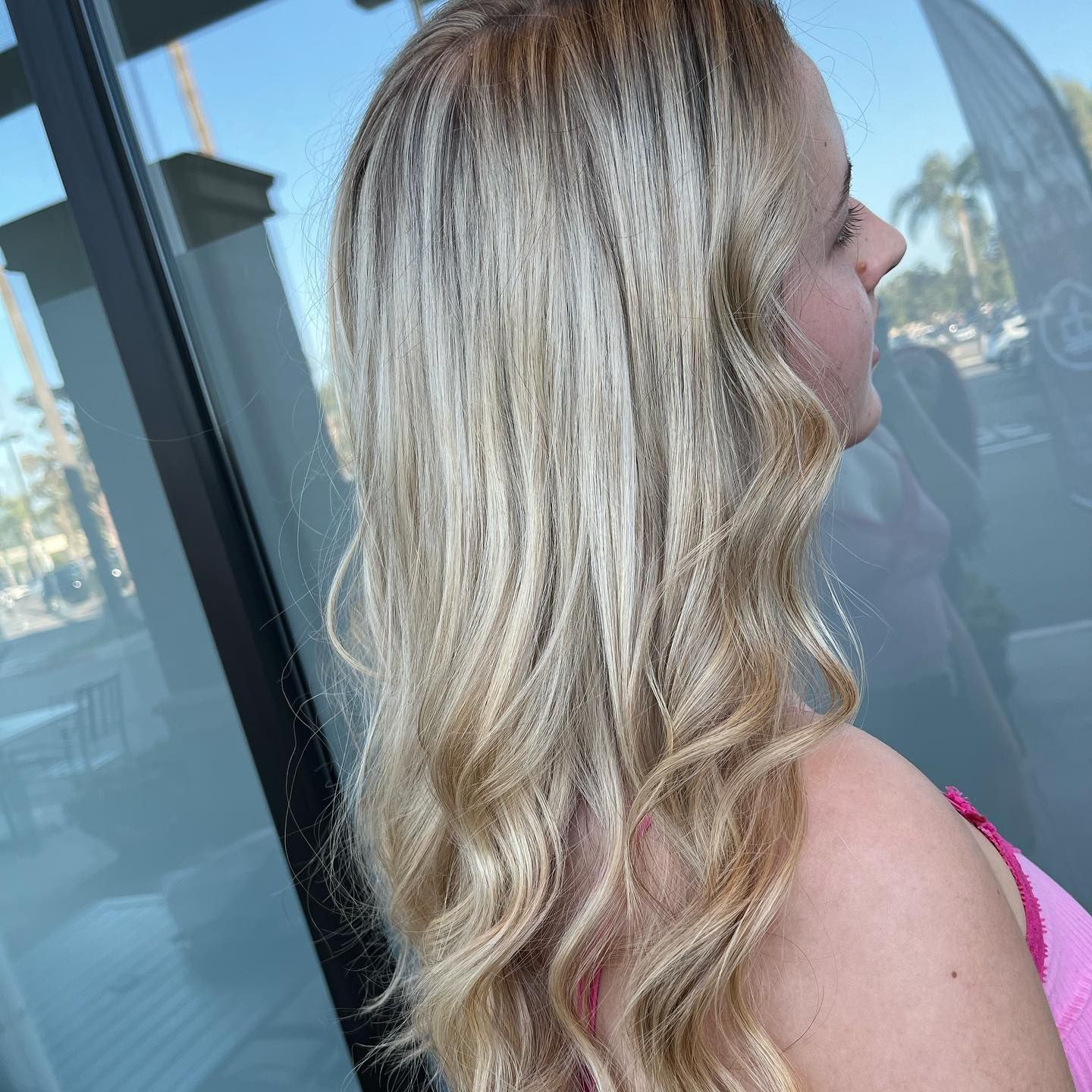 Woman with blonde wavy hair, wearing pink top, stands outside a building.