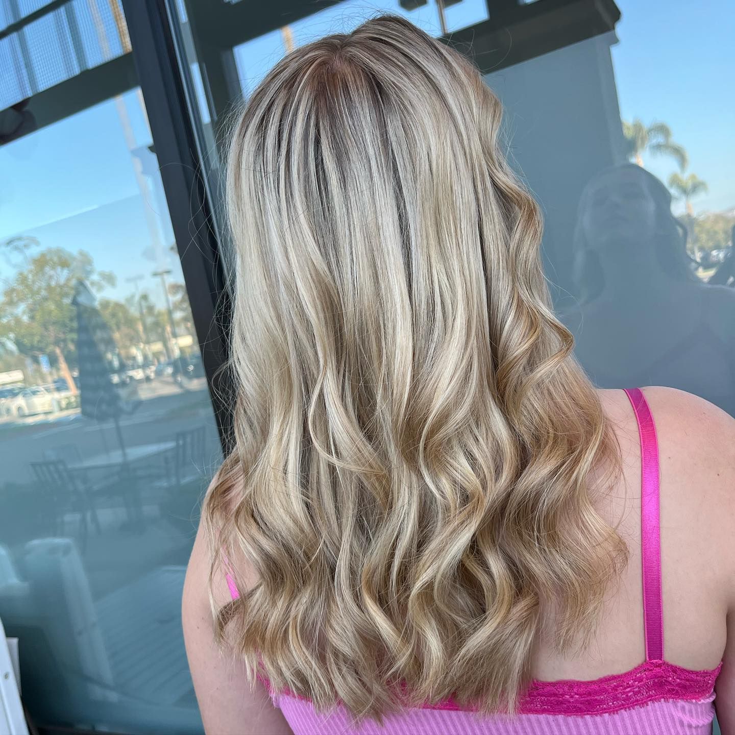 Woman with blonde wavy hair, wearing a pink top, outdoors.