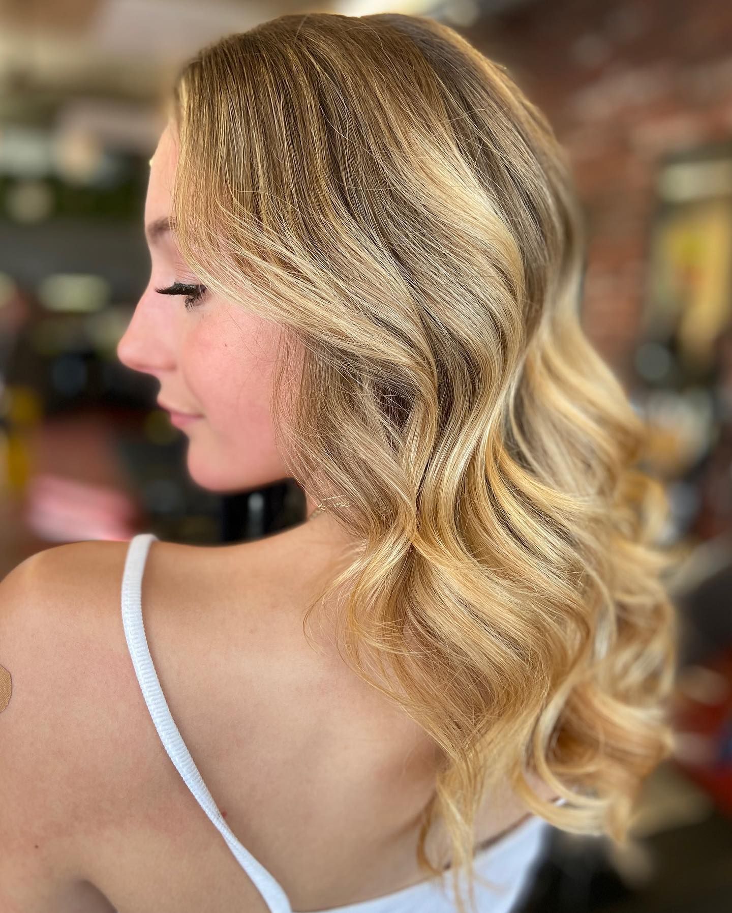 Woman with blonde hair styled in loose waves, wearing a white top, facing left.