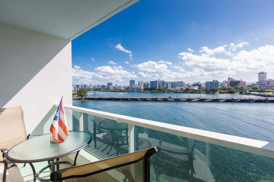 Balcony with glass railing overlooking a blue bay and city skyline under a bright sky