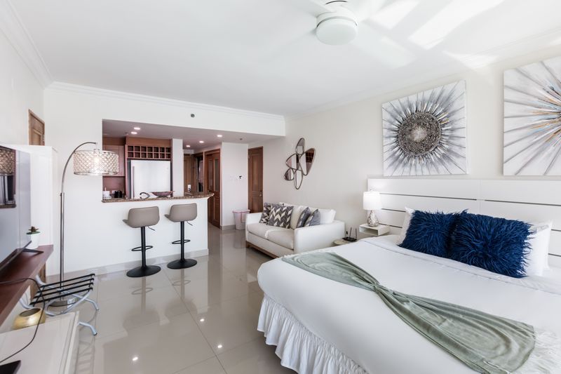 Bright modern studio apartment with bed, sofa, bar stools, and kitchenette